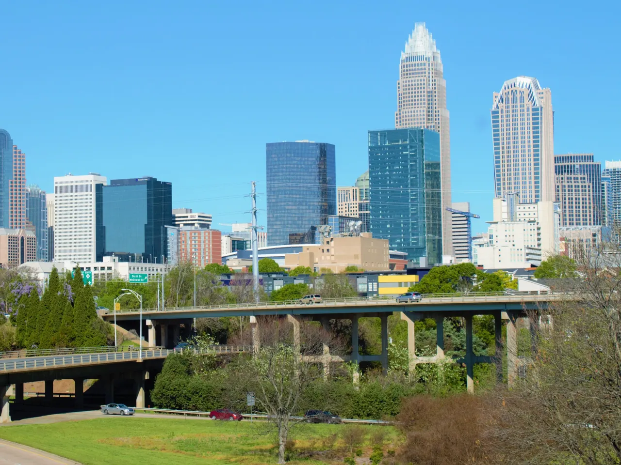 The towers of Uptown Charlotte, led by the Bank of America Corporate Center, above highway bridges and a green slope