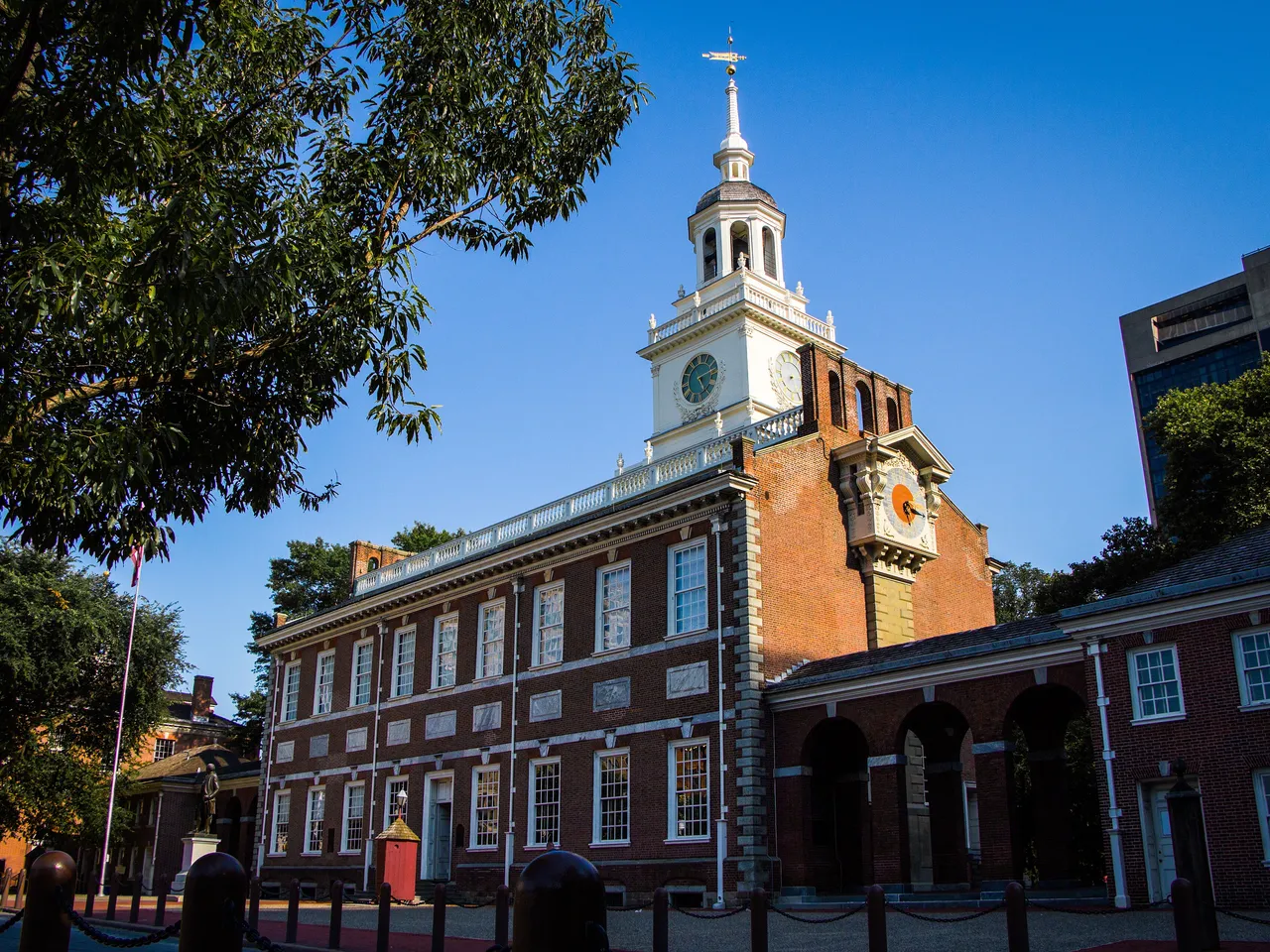 Independence Hall’s red-brick facade and white steeple under a clear blue sky, in Philadelphia